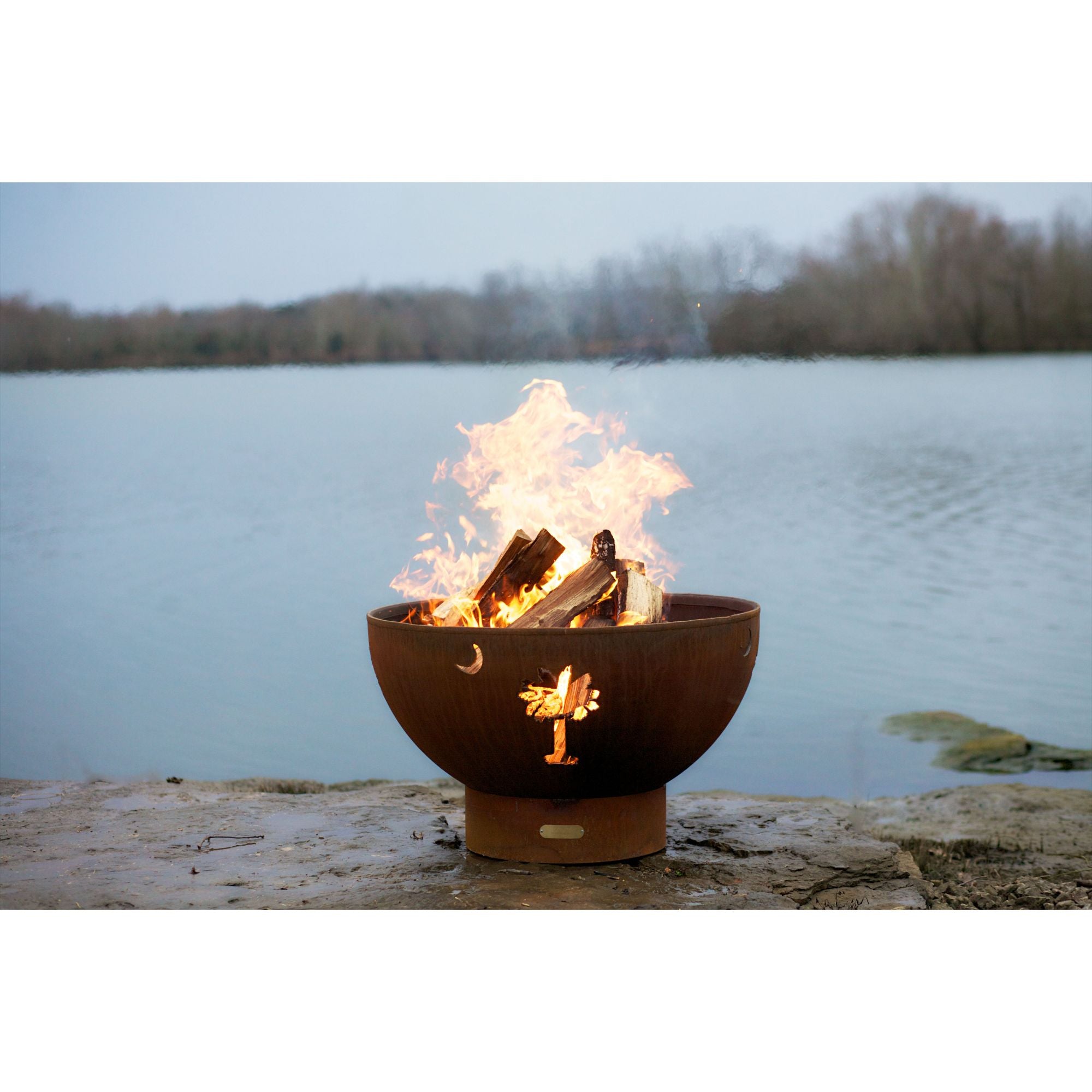 Fire pit with flames burning in it by a body of water