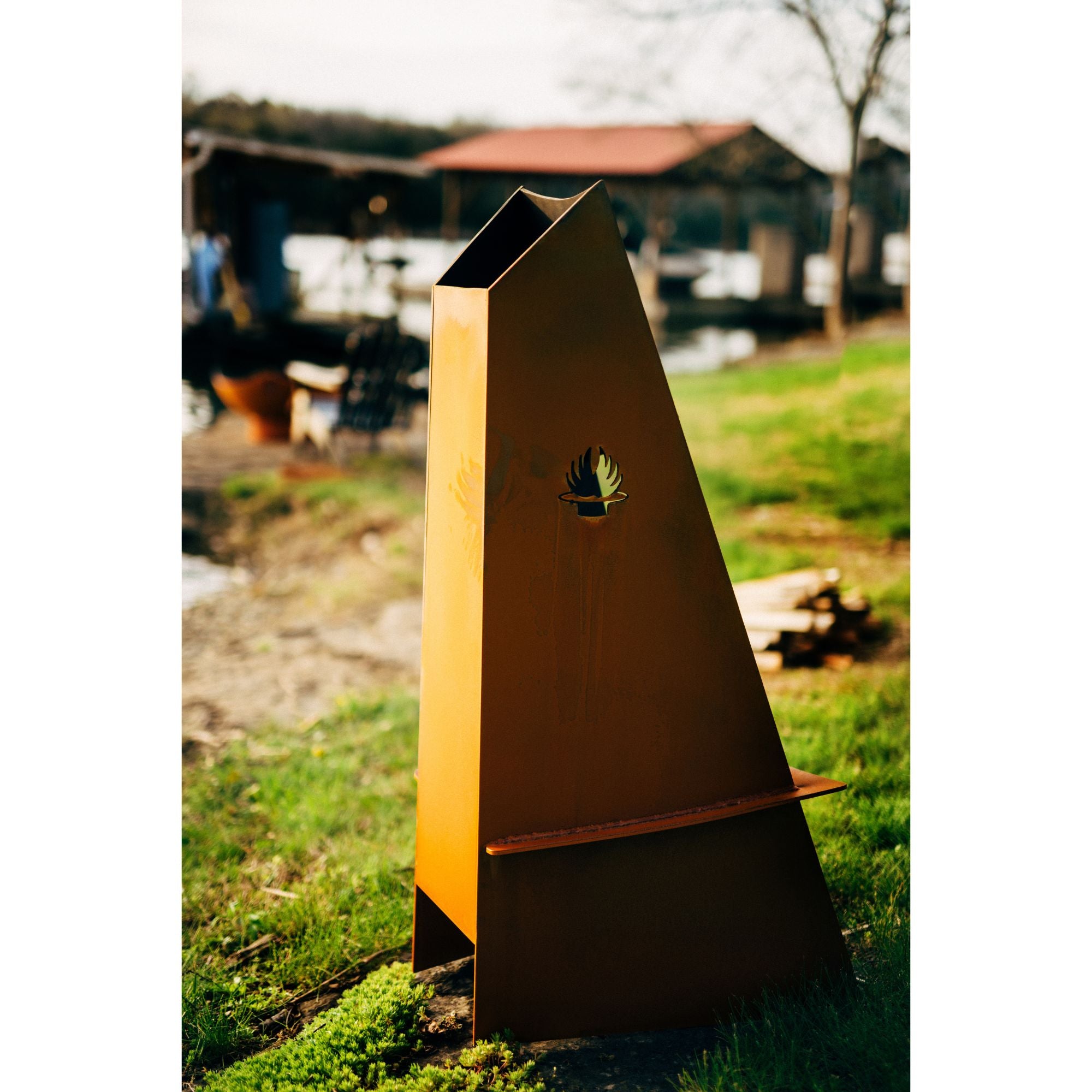 Metal fire pit shaped like a triangle on grass with a blurred background
