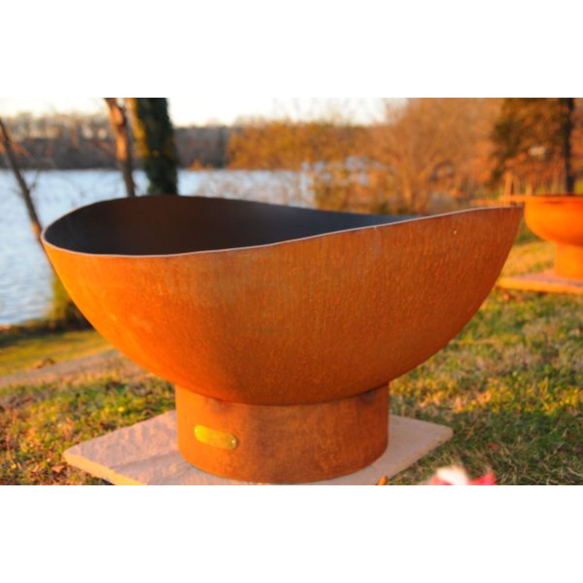 Rust-colored fire pit on a grassy area near a body of water.