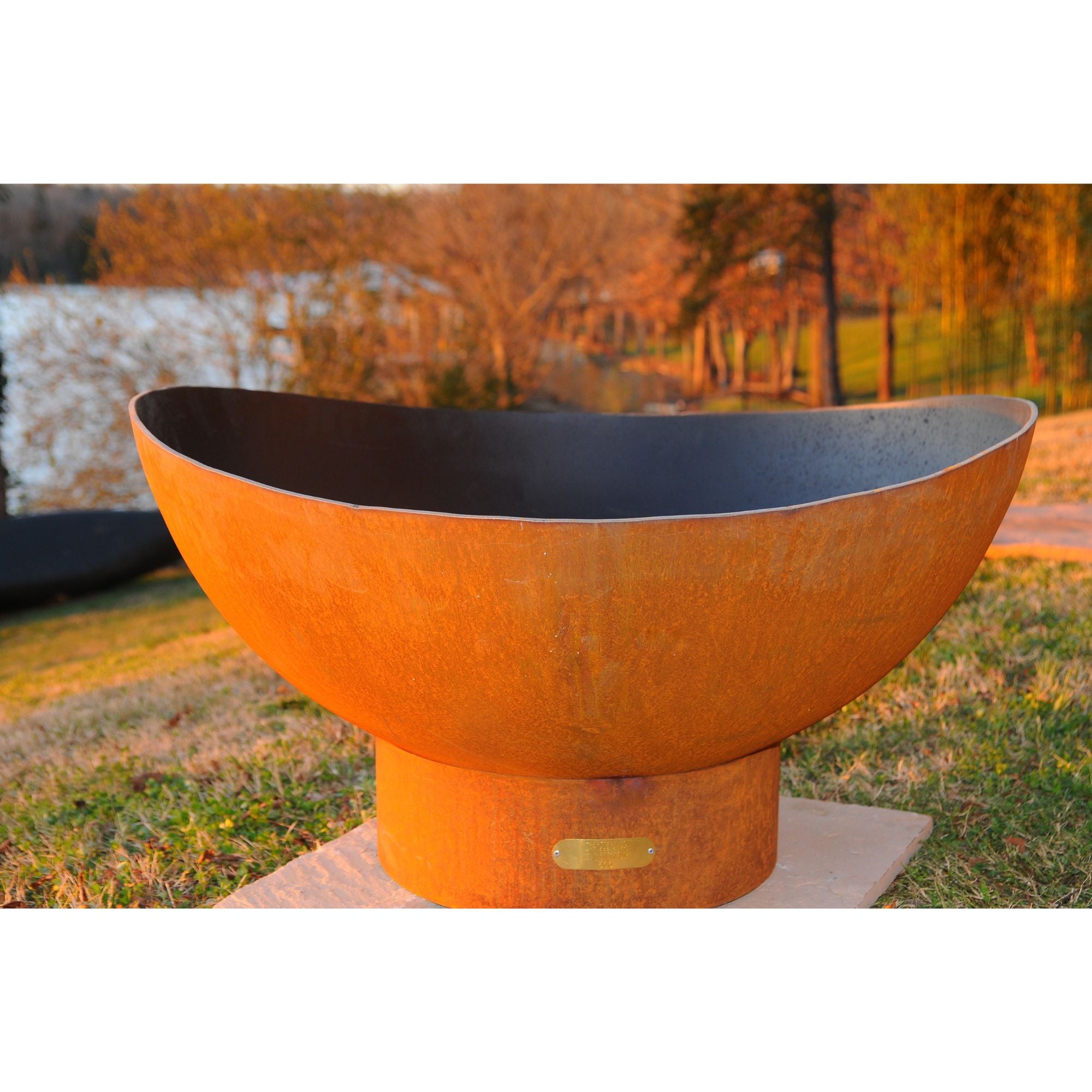 Rust-colored metal fire pit bowl on a grassy area with trees in the background