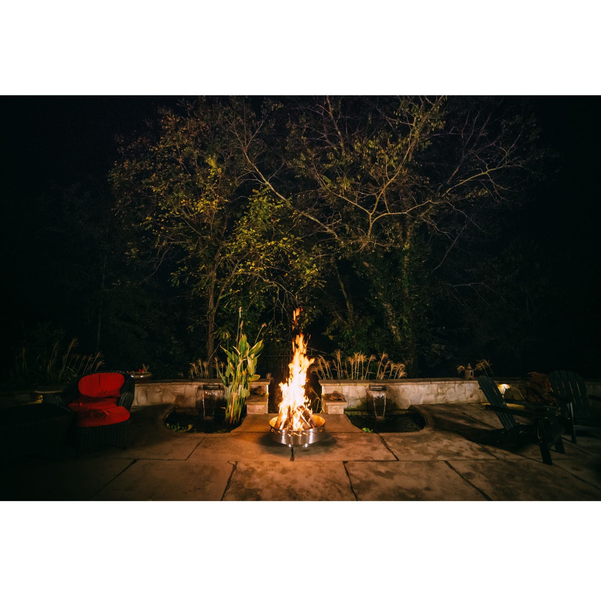 Fire pit in a garden setting at night with trees and benches.