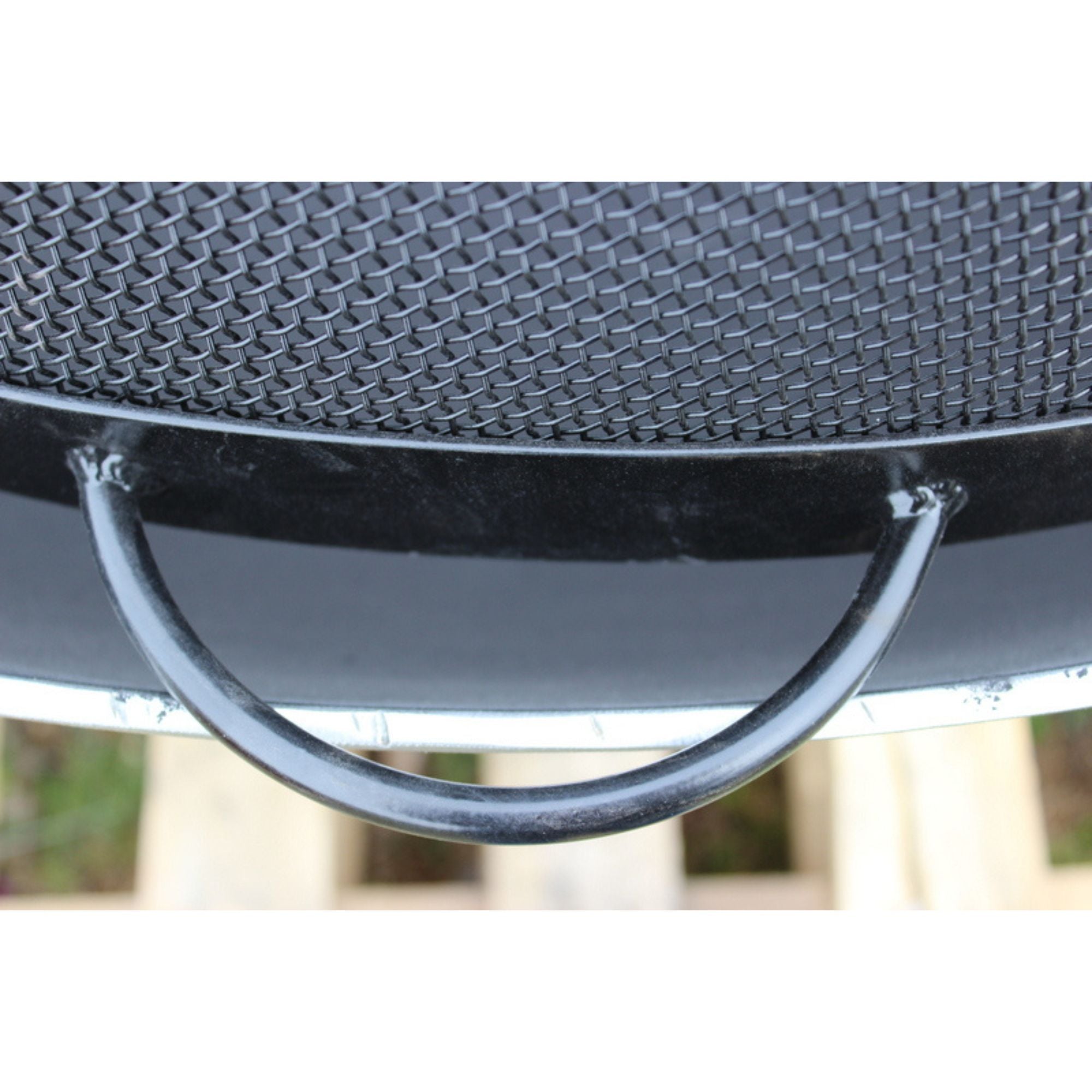 Close-up of a black fire pit spark guard with a metal handle on a blurred background