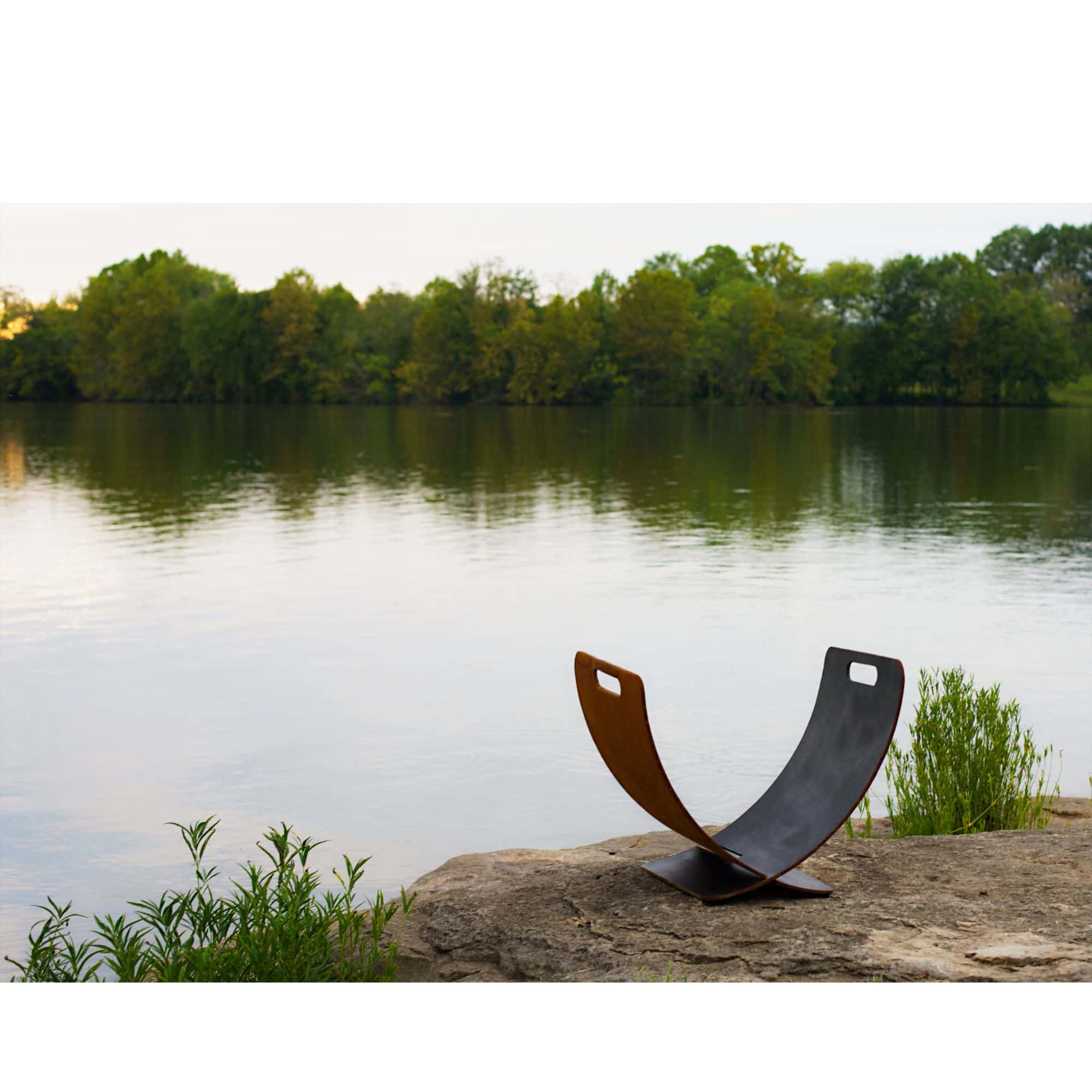 Modern steel log rack on a rock by a lake with trees in the background