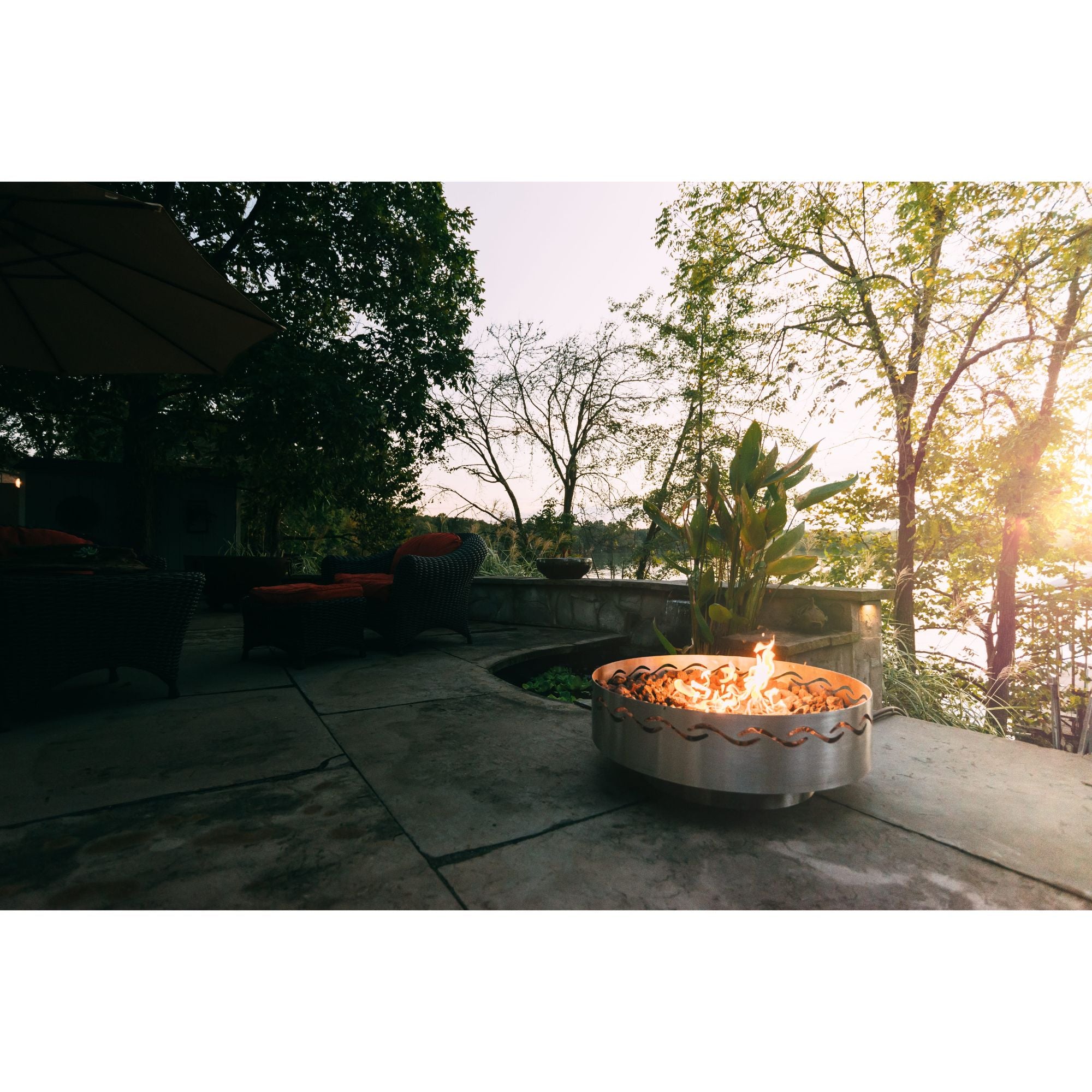Outdoor patio with a fire pit and seating area near trees and water.