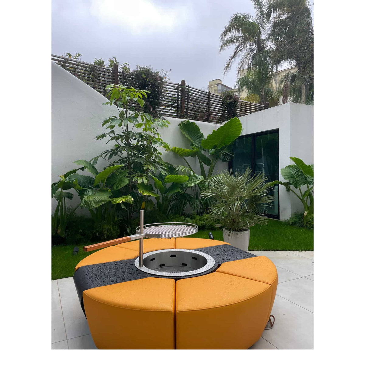 Round outdoor fire pit with orange and black design in a garden setting