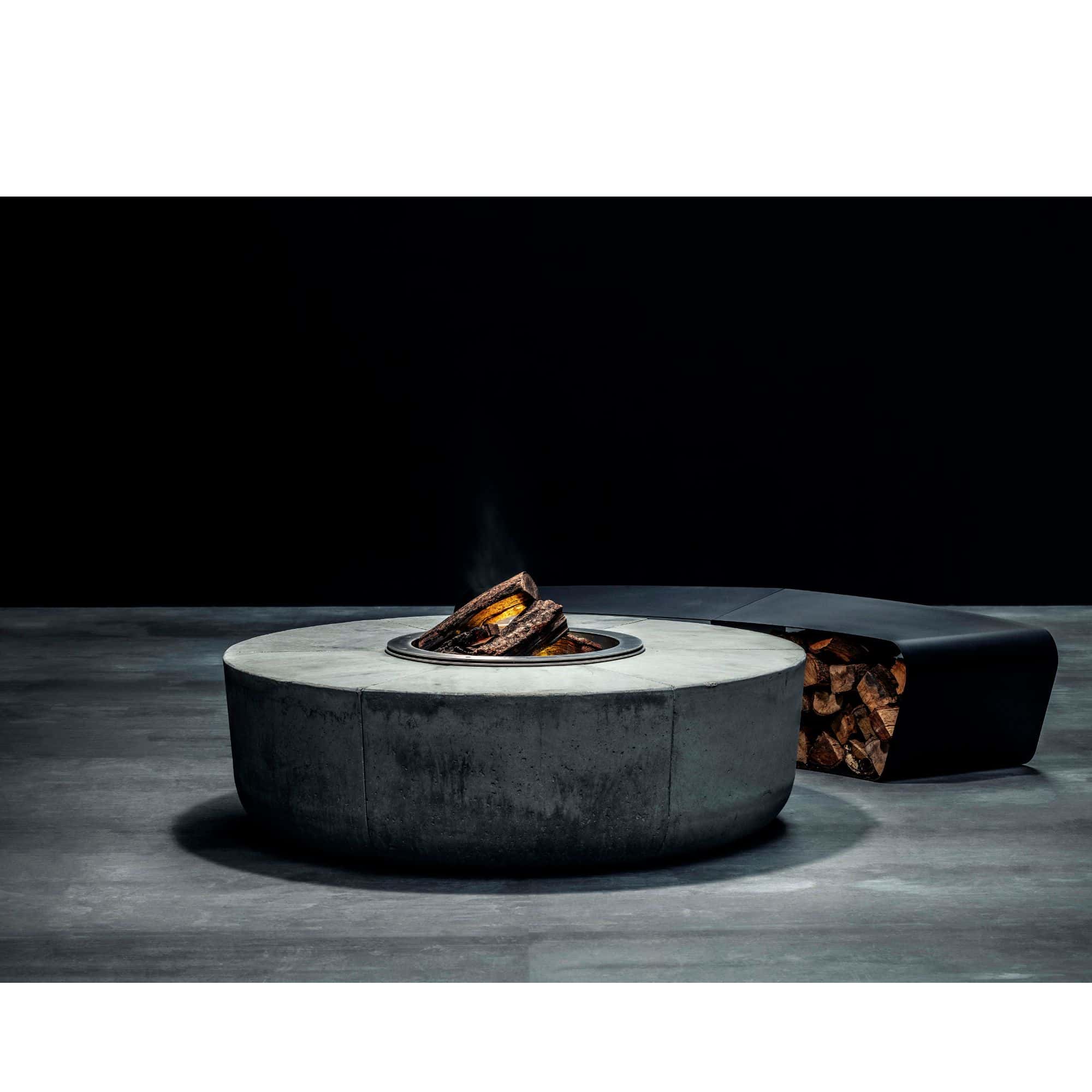 Concrete fire pit table with burning logs on a dark surface