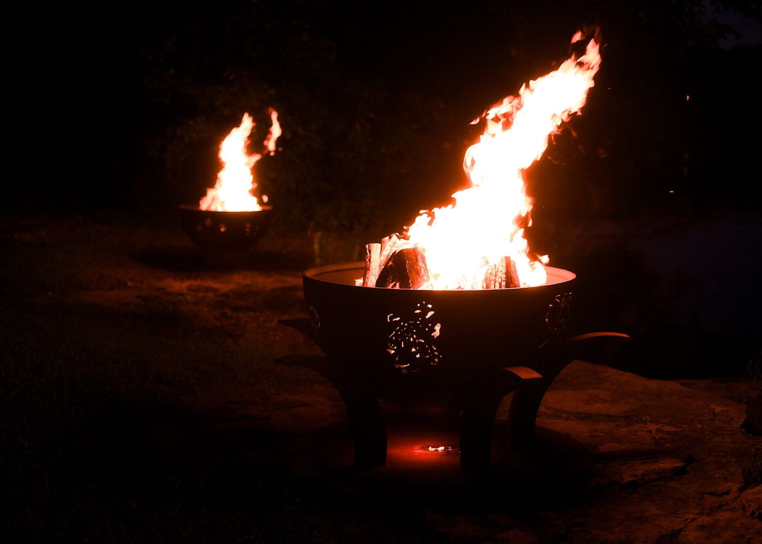 Two fire pits with flames burning brightly in the dark.