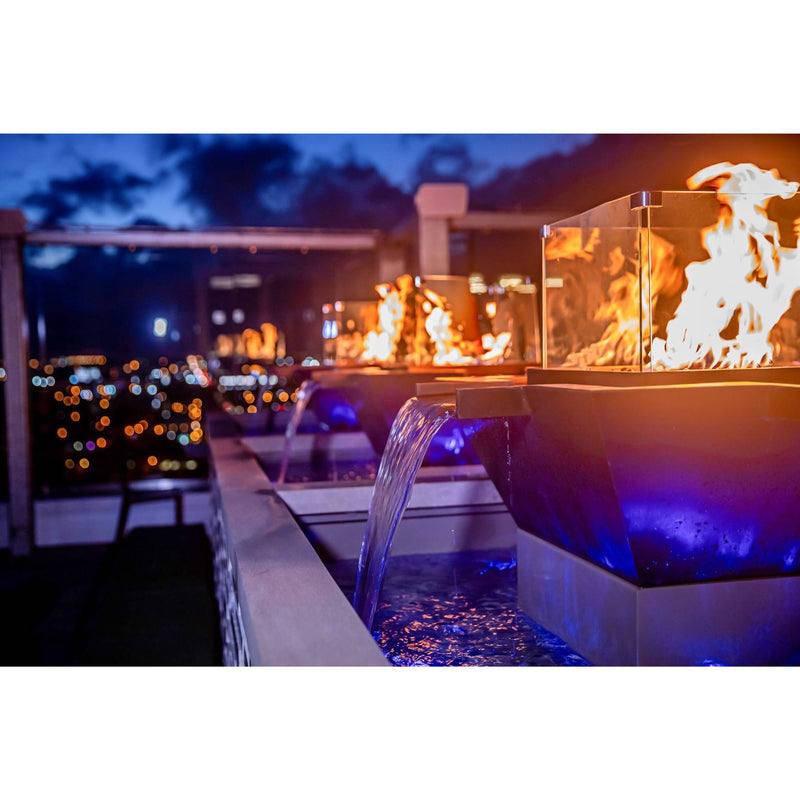 Outdoor setting with fire pits and water features at night, illuminated by blue and orange lights.