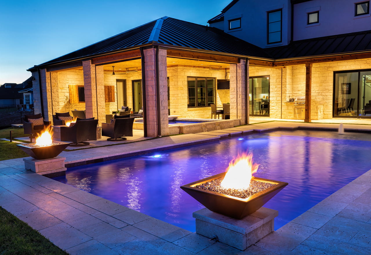 Evening view of a modern house with a pool and fire pits.