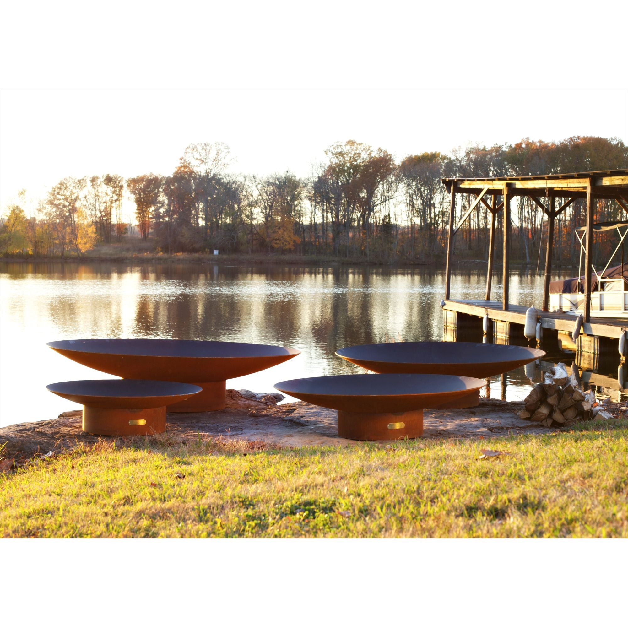 Outdoor fire pit area by a lake with trees and a dock in the background.