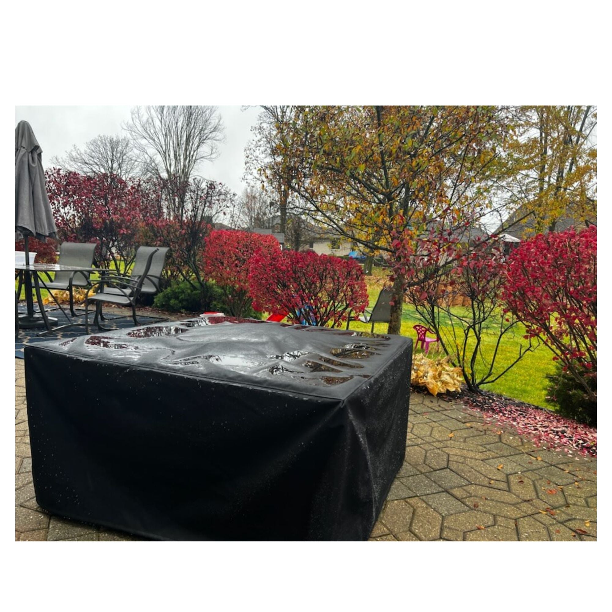 firepit covered with a black cover in an outdoor setting with trees and shrubs.
